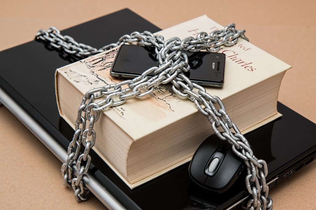 A book, computer, phone, and mouse, locked together by chain.